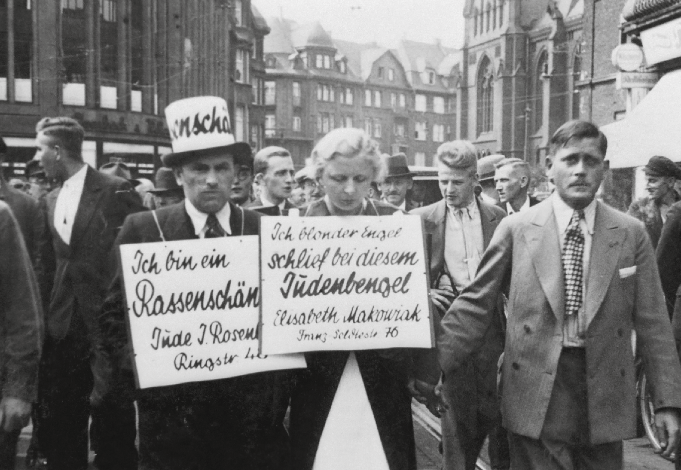 Schwarz-Weiß-Foto: Öffentliche Demütigung und Anprangerung von Juda Rosenberg und Elisabeth Makowiak, Menschen mit Plakaten mit antisemitischen Aussagen