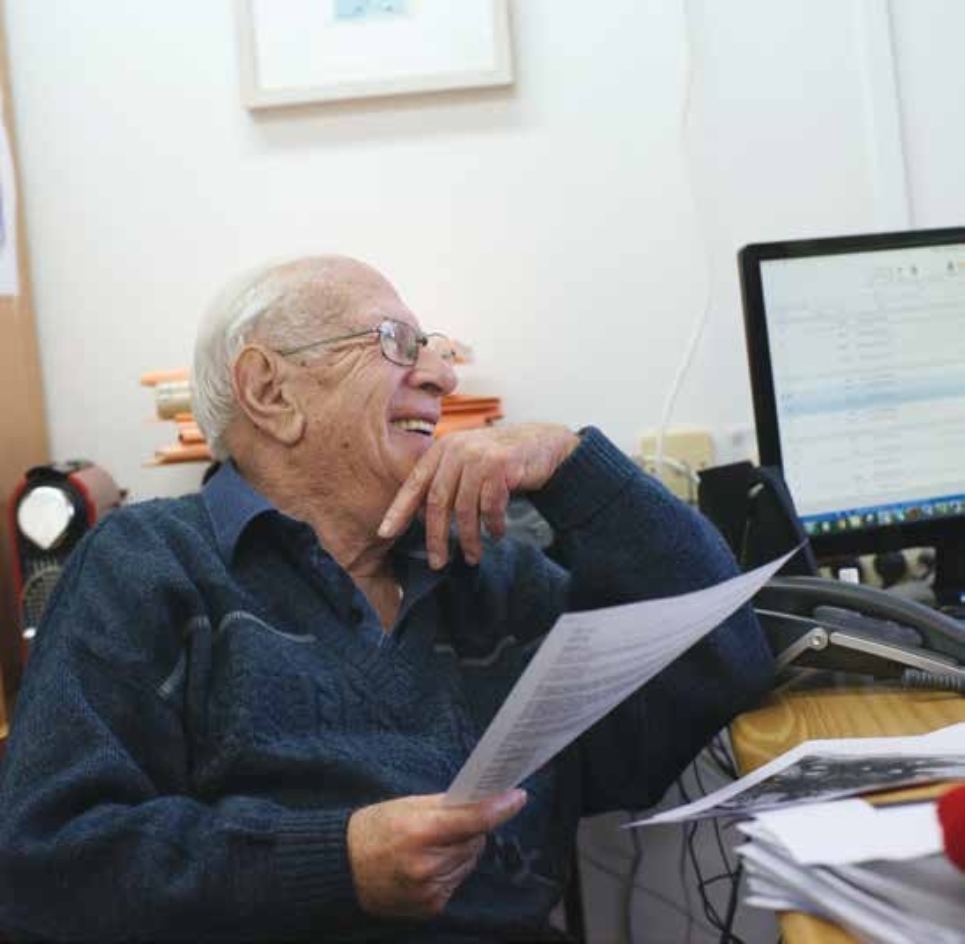Porträt von Moshe Kravec mit Zettel in der Hand neben Computer