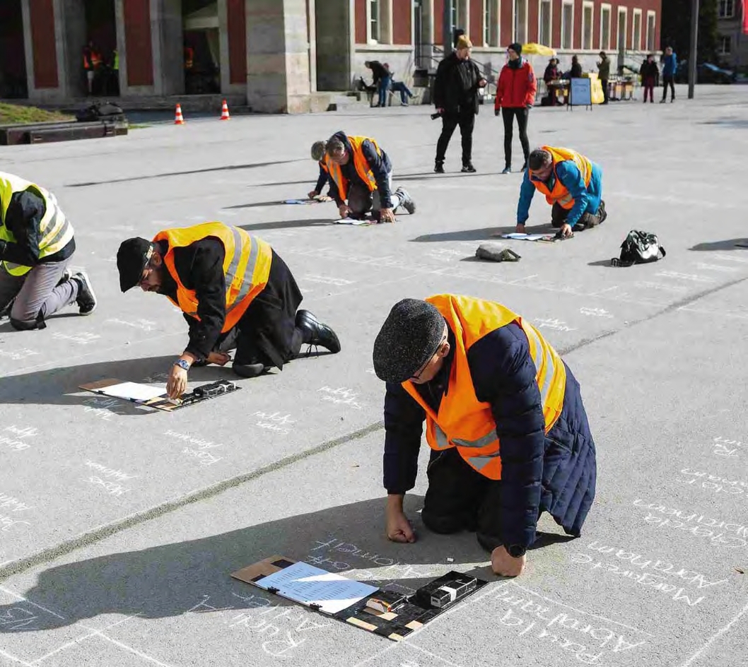 Männer in Warnwesten schreiben mit Kreide die Namen der Ermordeten auf den Stéphane-Hessel-Platz