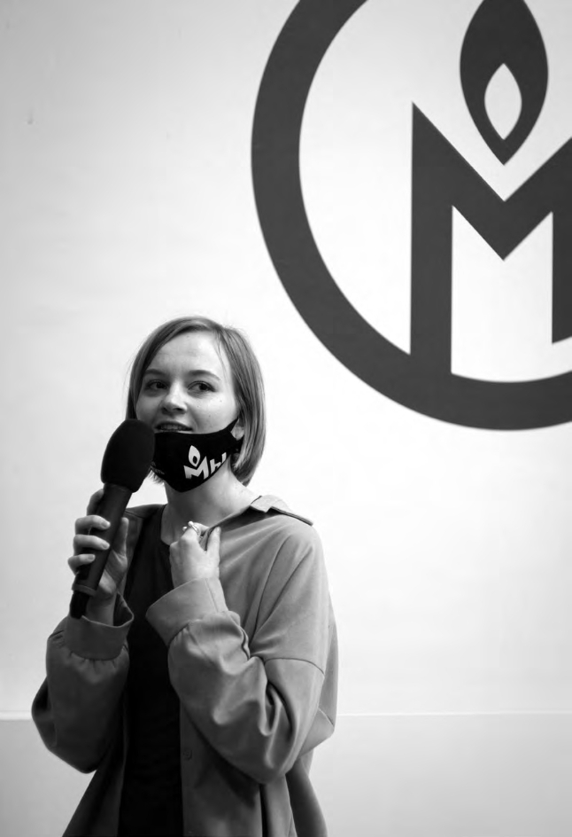 Schwarz-Weiß-Foto von Natalia Baryshnikova mit Mikrofon, hinter ihr auf der Wand das Memorial Logo