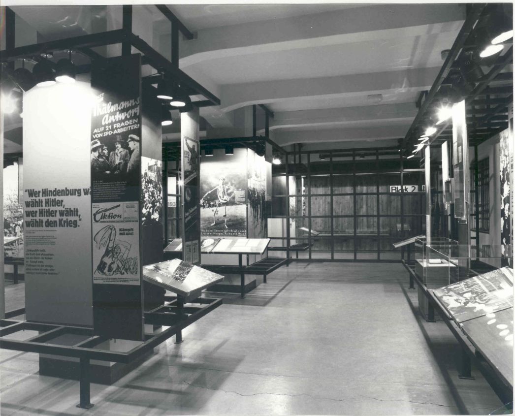Zu sehen ist Raum 1 im Museum des Antifaschistischen Widerstandskampfes. In der Mitte des Raumes sind Ausstekllungstafeln an Säulenartigen Metalgestellen angebracht. Vereinzelt sind Kommunistische Plakate aus der 1930er jahren zu erkennen.