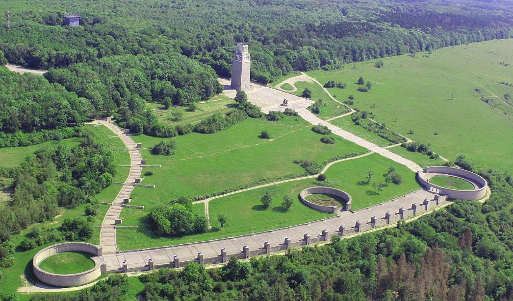 Das Mahnmal auf dem Gelände der Gedenkstätte aus der Luft fotografiert. Links oben beginnt der Stelenweg bergab. Weiter unten führt die Straße der Nationen von einem Ringgrab zum nächsten. Auf halber Strecke sieht man noch ein weiteres Ringgrab. Von dort führt der Weg bergauf zum Glockenturm.
