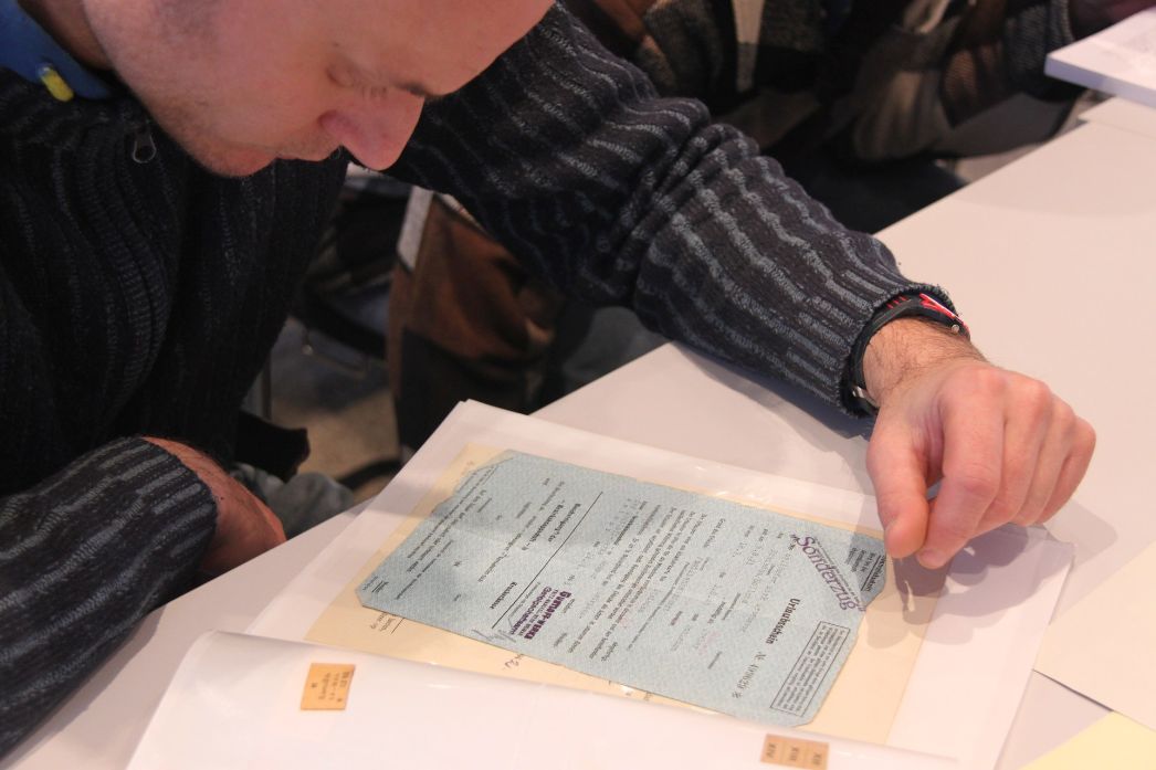 The picture shows a young man bent over a document file lying on the table. These are documents of former forced labourers.