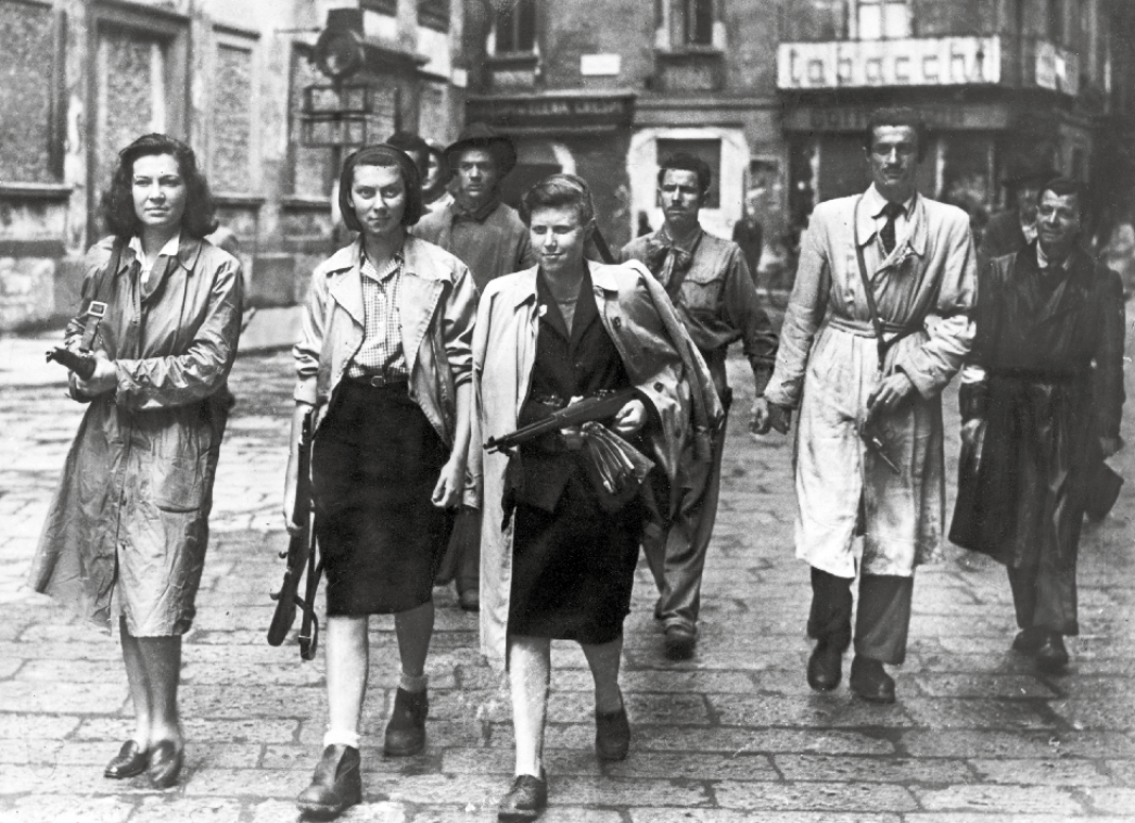 Schwarz-Weiß-Fotografie: im Vordergrund sind drei Frauen mit Gewehren zu sehen, im Hintergrund einige Männer.
