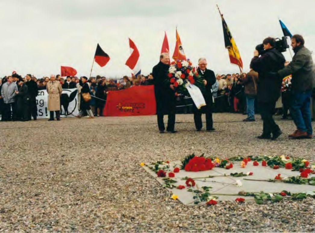 Auf dem Appellplatz Buchenwalds vor der Gedenkplatte: Menschenmenge sowie Pierre Durand und Guy Ducoloné, die einen Kranz tragen.