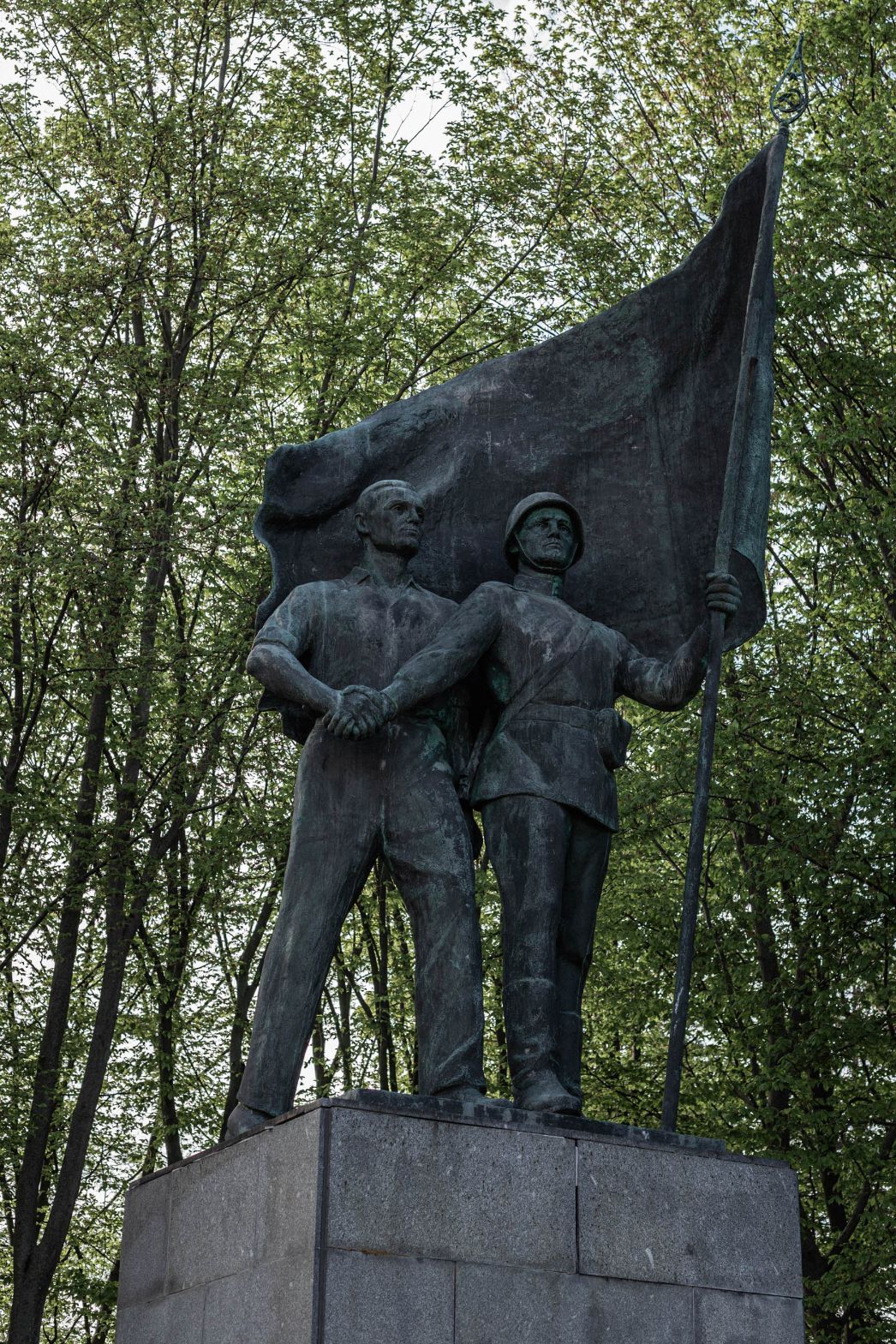 Sowjetisches Ehrenmahl. Soldat hält Flagge, mit der anderen Hand drückt er die Hand eines Arbeiters, der hinter ihm steht.