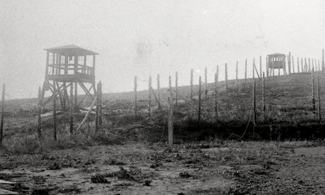 Schwarz-Weiß-Foto: Ansicht des Lagerzauns und zweier Wachtürme des ehemaligen KZ Mittelbau-Dora