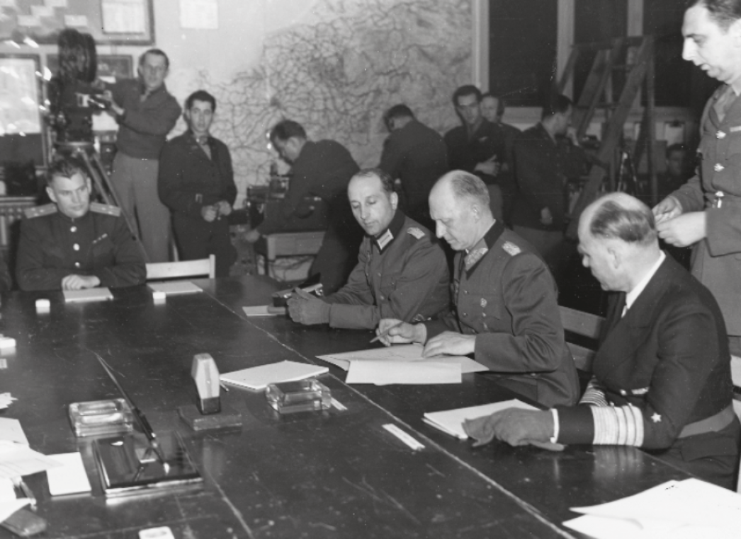 Dieses historische Foto zeigt die Unterzeichnung der bedingungslosen Kapitulation der deutschen Wehrmacht am 8. Mai 1945 (nach mitteleuropäischer Zeit) in Reims, Frankreich – eines der entscheidenden Ereignisse zur Beendigung des Zweiten Weltkriegs in Europa. 📜 Abgebildete Szene: Am Tisch sitzen hochrangige Vertreter der Wehrmacht und der Alliierten: In der Bildmitte unterschreibt Generaloberst Alfred Jodl, Chef des Wehrmachtführungsstabes, im Namen der deutschen Streitkräfte. Links von ihm: Generaladmiral Hans-Georg von Friedeburg (Kriegsmarine). Ganz rechts (mit Handschuhen): Generalmajor Wilhelm Oxenius, Jodls Adjutant. Links am Tisch: ein sowjetischer Offizier (Beobachter). Im Hintergrund: alliierte Offiziere, Beobachter, Techniker und Kamerateams dokumentieren das Geschehen.