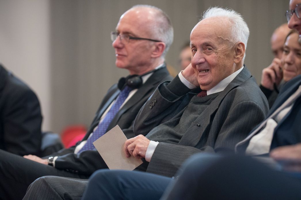 Auf dem Foto ist der Holocaust-Überlebende und Schriftsteller Ivan Ivanji bei einer Veranstaltung in späteren Lebensjahren zu sehen. Er sitzt lächelnd im Publikum, gut gekleidet in Anzug und Krawatte. Die entspannte Geste und sein freundlicher Ausdruck vermitteln Würde, Lebenserfahrung – und zugleich eine gewisse Gelassenheit.