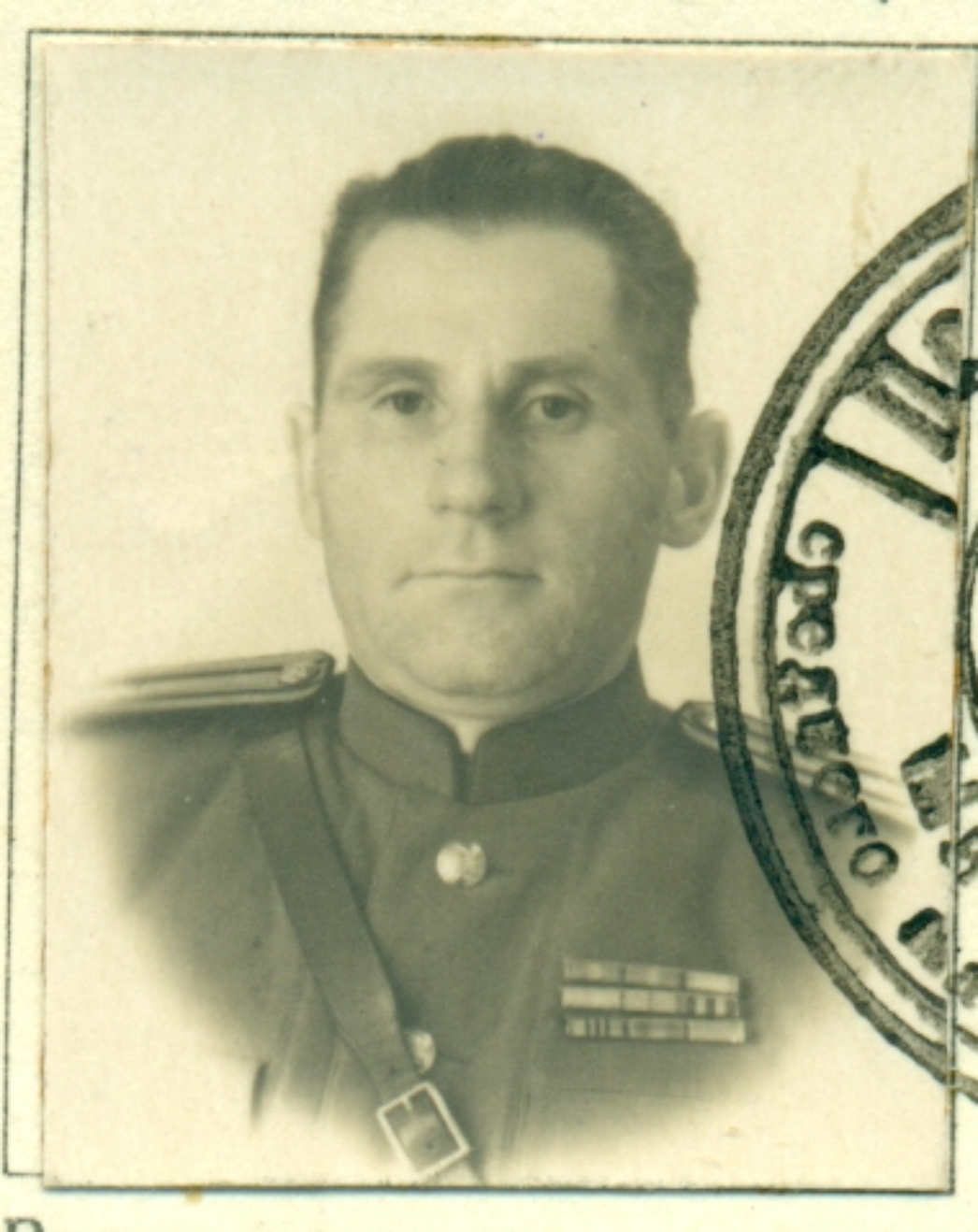 Schwarzweißes Porträt eines Mannes in militärischer Uniform. Er blickt frontal in die Kamera und trägt eine Jacke mit Schulterklappen und mehreren Ordensbändern auf der Brust. Rechts im Bild ist ein teilweise sichtbarer Stempelabdruck zu erkennen, der auf ein offizielles Dokument hinweist.