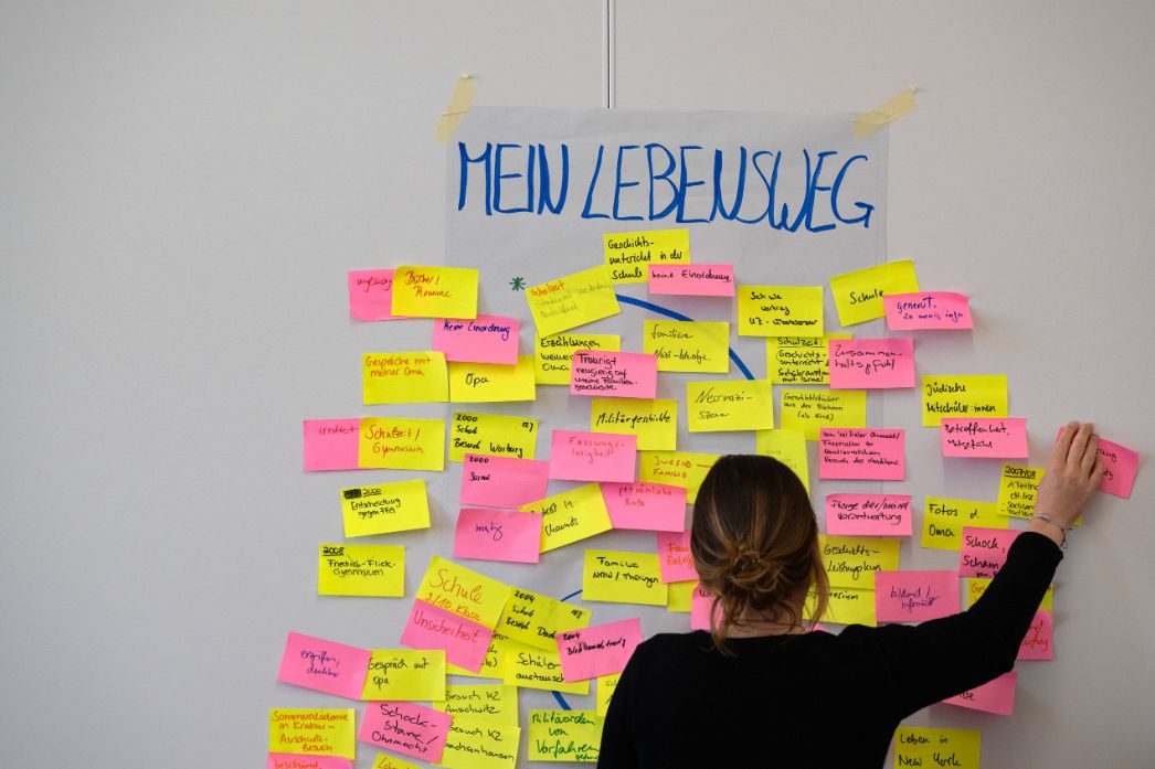 Eine Person ergänzt ihren „Lebensweg“ auf einer Wand mit vielen farbigen Notizzetteln.
