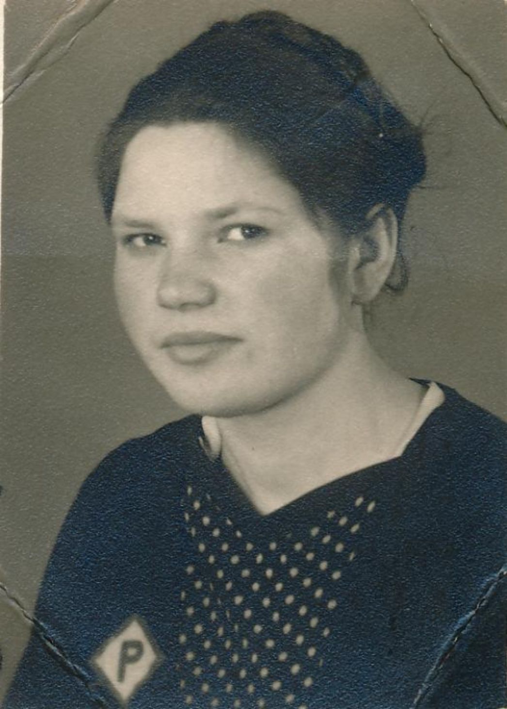 Ein historisches Porträt zeigt eine junge Frau mit ernstem Blick. Das Foto ist gealtert und weist Gebrauchsspuren auf, was auf seine lange Überlieferungsgeschichte hinweist. Auf ihrer Kleidung ist ein Abzeichen mit dem Buchstaben "P", was ein ein Kennzeichen für polnische Zwangsarbeiter war.