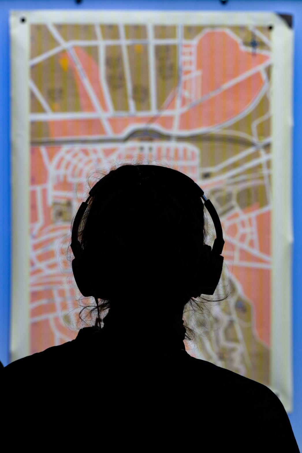 Eine Person betrachtet mit Kopfhörern eine Karte in der Ausstellung. Die Silhouette vor dem beleuchteten Exponat verweist auf ein individuelles, vertieftes Hörerlebnis.