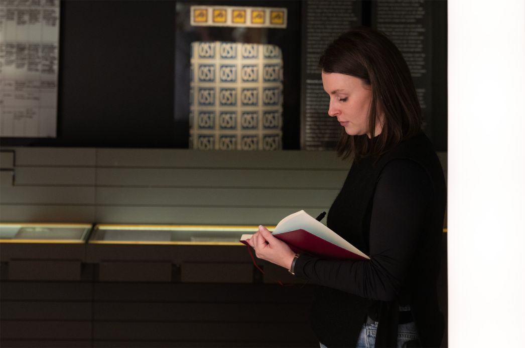 Eine Frau steht nachdenklich in der Ausstellung und macht sich Notizen.