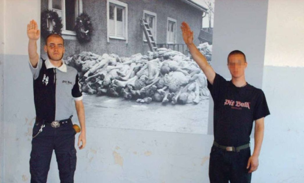 Zwei Männer machen den Hitlerguß vor dem Bild eines Leichenberges