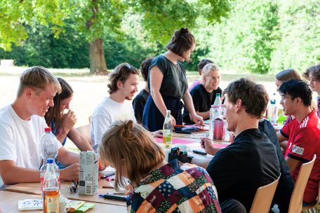 A group of young participants in a multi-day program working outside at a long work table on various educational materials.