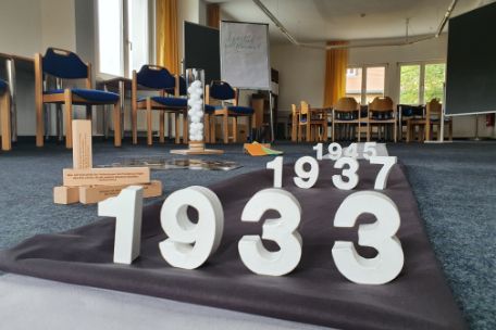 View into a seminar room. On the floor is a gray cloth, on it the dates 1933, behind it 1937 and 1945. In the background chairs and tables can be seen.