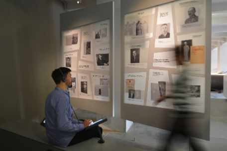 A man sits at a listening station in the Buchenwald permanent exhibition, looking at a display case while wearing headphones on his ears. 