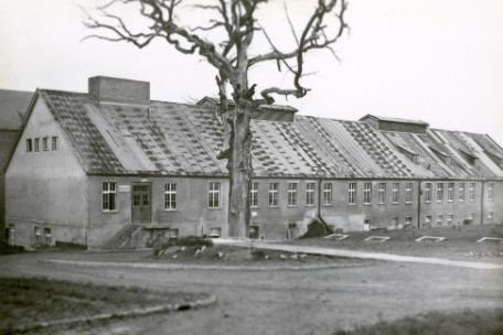Gebäude der Häftlingswäscherei. Ein langes, zweistöckiges Gebäude schlichtester Architektur mit hohem Giebeldach. Im Vordergrund die blätterlose Goethe-Eiche.