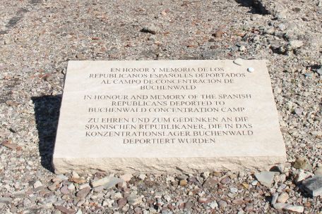 Weißer Gedenkstein mit dem Schriftzug Schriftzug: "Zu Ehren und zu Gedenken an die spanischen Republikaner, die in das Konzentrationslager Buchenwald deportiert wurden“ Auf spanisch, englisch und deutsch. 