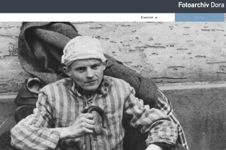 Screenshot of the homepage of the Digital Photo Archive of the Mittelbau-Dora Concentration Camp Memorial. A large photo shows a prisoner in striped clothing sitting against a concrete wall. 