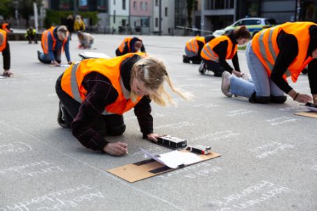 Teilnehmende schreiben mit Kreide die Namen der Ermordeten auf den Stéphane-Hessel-Platz