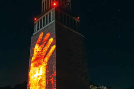 Dieses Bild zeigt den Glockenturm der Gedenkstätte Buchenwald bei Nacht – eindrucksvoll illuminiert mit einer riesigen roten Hand, die über die gesamte Turmfassade projiziert wird. Die Lichtinstallation erzeugt eine starke visuelle und emotionale Wirkung.