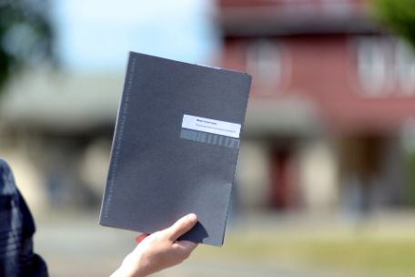 A person, of whom only the hand can be seen, holds up a folder with the title "Application Folder".