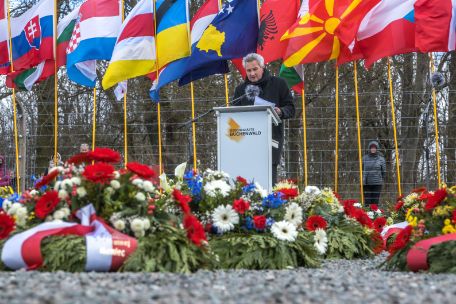 Jens-Christian Wagner at a lectern. Behind him flags and the camp fence, in front of him numerous wreaths. 
