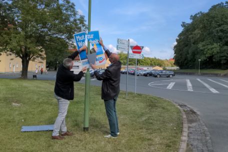The photo shows two men taking down an AfD poster with the slogan "Courage for truth".