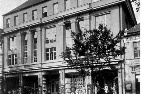 Black and white photo of an old building with "KAUFHAUS" sign and cobbled street in the foreground.