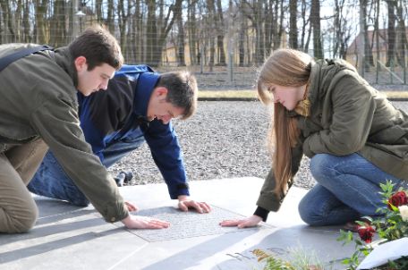 Three young visitors touch the heated metal square memorial sign on the roll call square.