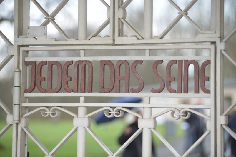 Blick auf das weiße Lagertor mit dem von innen lesbaren Schriftzug "Jedem das Seine" in soten Buchstaben