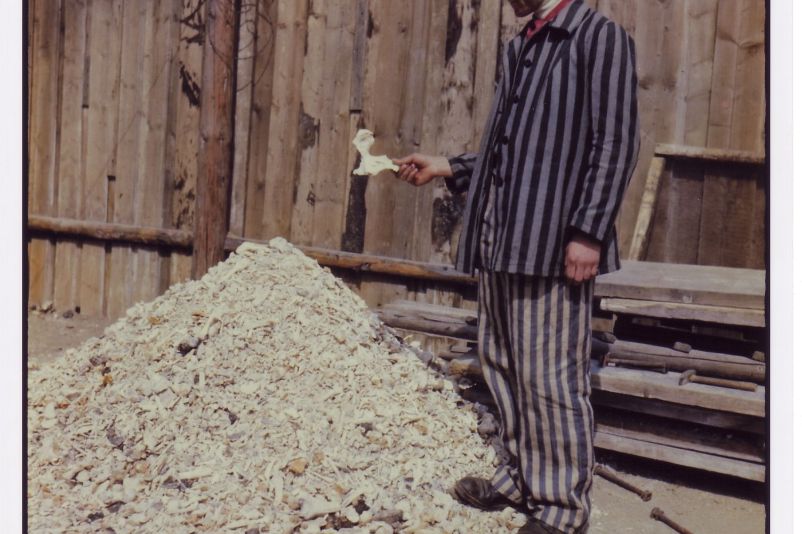 Ein Häftling des Konzentrationslagers Buchenwald hält einen menschlichen Knochen, während er vor einem Knochenhaufen steht, der aus einem Krematorium geschaufelt wurde.