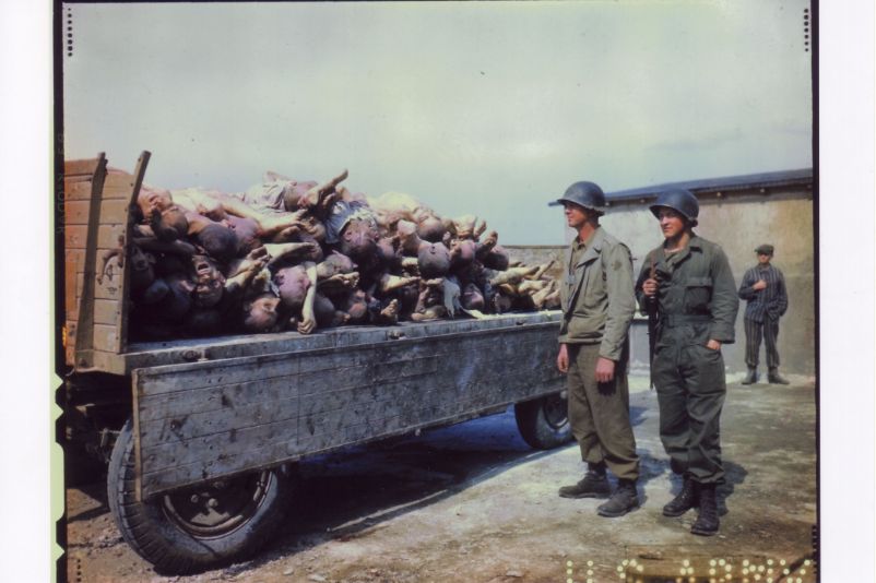 Two American soldiers in front of a trailer with corpses in the courtyard of the crematorium. In the background a liberated prisoner