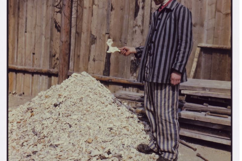 A prisoner of Buchenwald concentration camp holds a human bone while standing in front of a pile of bones shoveled from a crematorium.